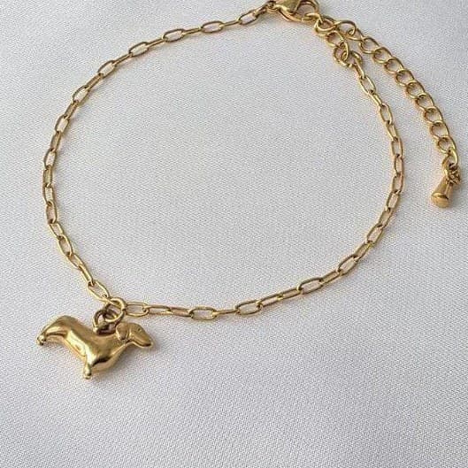 Originalfoto: goldenes Gliederarmband mit Dackelanhänger auf hellem Stoff