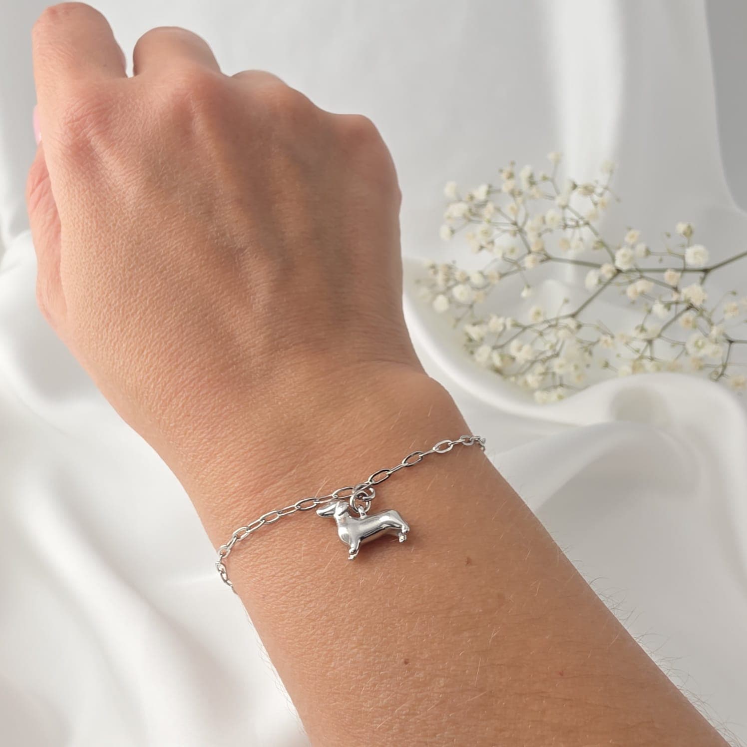 Originalfoto: Silberarmband mit Dackelanhänger am Handgelenk vor weißem Stoff mit Schleierkraut